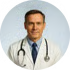 A doctor with a stethoscope, wearing a white coat and blue tie, smiles against a light background.